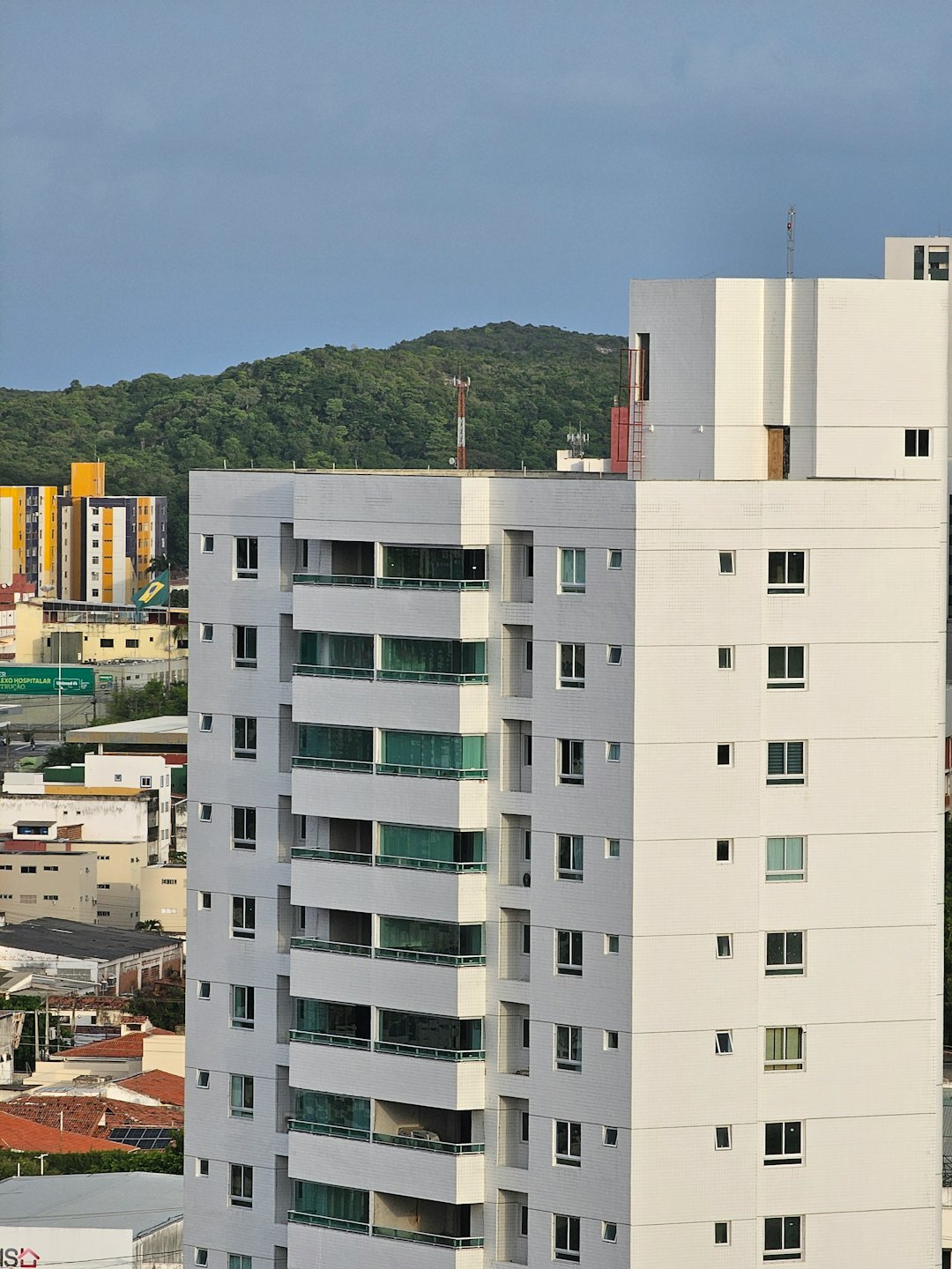 Modern white apartment buildings sit before a lush green hill.